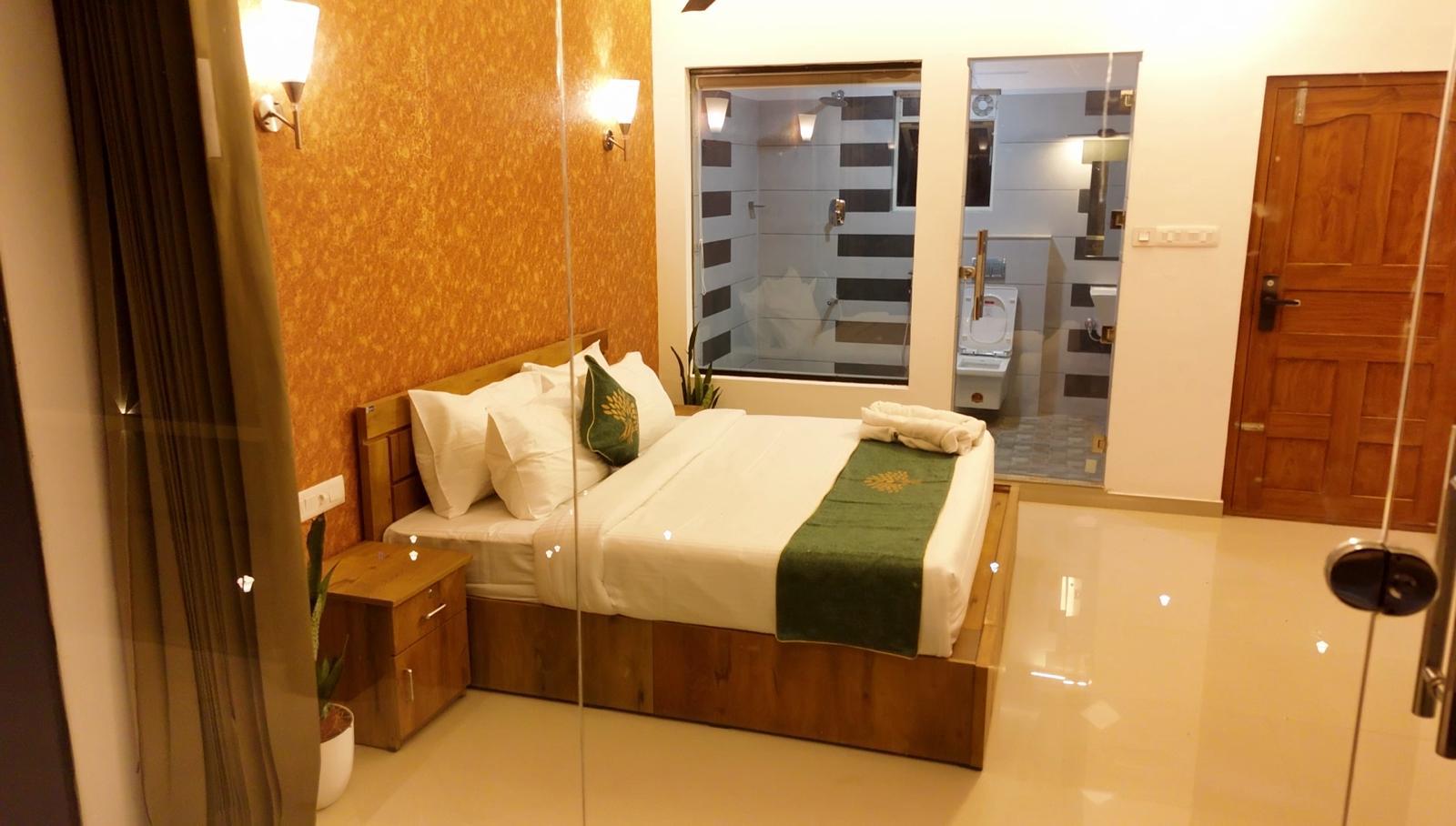 Hotel manager stands in a modern, well-lit office, smiling confidently with arms crossed. The background features large windows, green plants, and a desk with neatly arranged documents, conveying professionalism and approachability. No visible text. The mood is welcoming and competent.