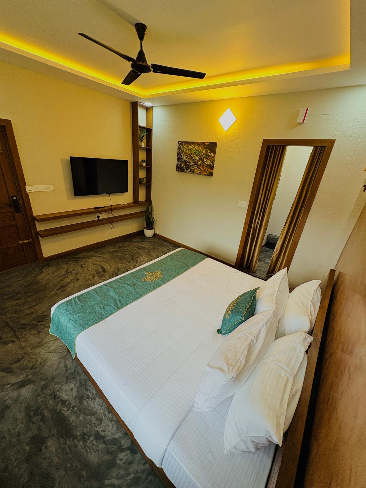 Luxury suite room at JKR Gardens Resort with modern decor, king-size bed, ambient lighting, wooden furniture, and a view of the bathroom through a glass door. No visible text.